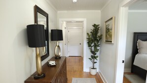 Ein Korridor mit Holzboden, einem gemusterten Teppich, einer Zimmerpflanze und zwei Lampen auf einer Holzkonsole.