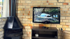 A brick wall with a television mounted on it, a black chimney, and a wooden beam. - Casa Rosa Beat No Coração do Rosa (Imbituba)