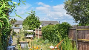 Un giardino con recinzione in legno, un tavolo e sedie, e diverse piante e fiori.