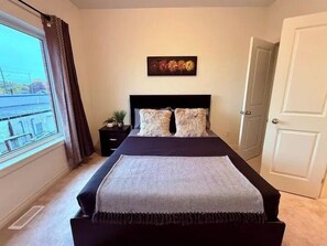 A bedroom with a bed, a nightstand, a window with curtains, and a door. - Ajax Villa  (Ajax)