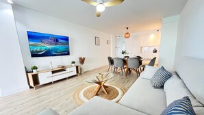 Un salon moderne doté d’un grand téléviseur à écran plat, d’un canapé, d’une table basse et d’un coin repas avec des chaises.