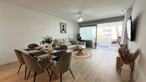 Un salon moderne avec une table à manger en verre, un canapé et un téléviseur fixé au mur.