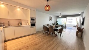 Une cuisine moderne avec des meubles blancs, un coin repas comprenant une table et des chaises, et une grande fenêtre donnant sur un patio.
