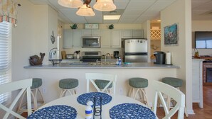 Una cocina con armarios blancos, una isla central con taburetes y una mesa de comedor con individuales azules.