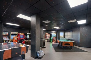 A pool table, arcade games, and a billiards table in a room with a dark ceiling and walls. - Sunrise & Serenity - St. Regis Condo #3001 (N. Topsail Beach)