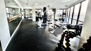Un gimnasio con equipo de ejercicio, ventanas amplias y un espejo en la pared.