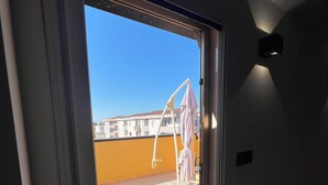 A view through a sliding glass door to an outdoor balcony with a tiled floor, a white metal chair, and a building in the background. - Relax by the Sea – Cozy 2-Bedroom Apartment with Terrace in Campomarino lido (Campomarino)