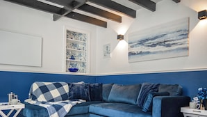 A corner living room with a blue sectional sofa, a white coffee table, a blue and white checkered throw blanket, a white side table, and a blue vase. - 2 bedroom accommodation in Staithes (Staithes)