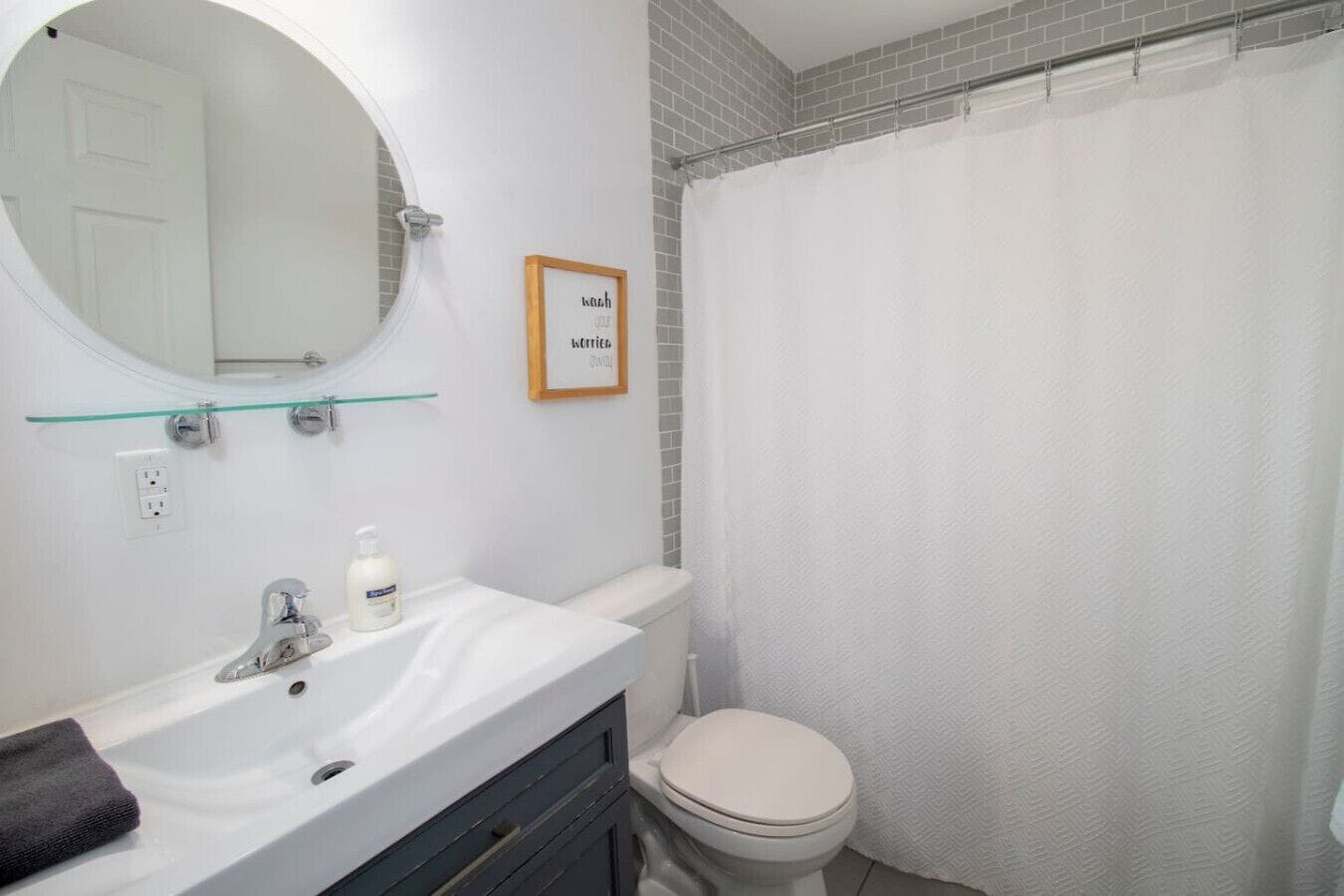 Ein Badezimmer mit einem weißen Waschbecken, Spiegel und Toilette. Ein Duschvorhang und ein gerahmtes Schild sind an der Wand angebracht.