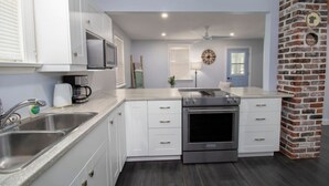 A modern kitchen with white cabinets, stainless steel appliances, and a brick accent wall. - The Little Lake House-Cozy 2Bdrm (Midland)
