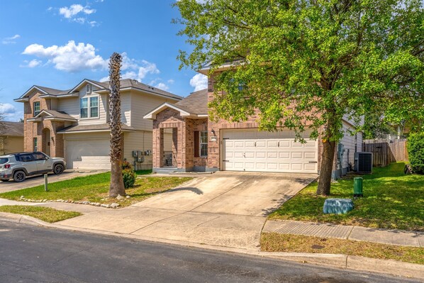 A two-story house with a garage, a driveway, and a lawn. - Spacious 4 BR | Near Med Center & Lackland (San Antonio)