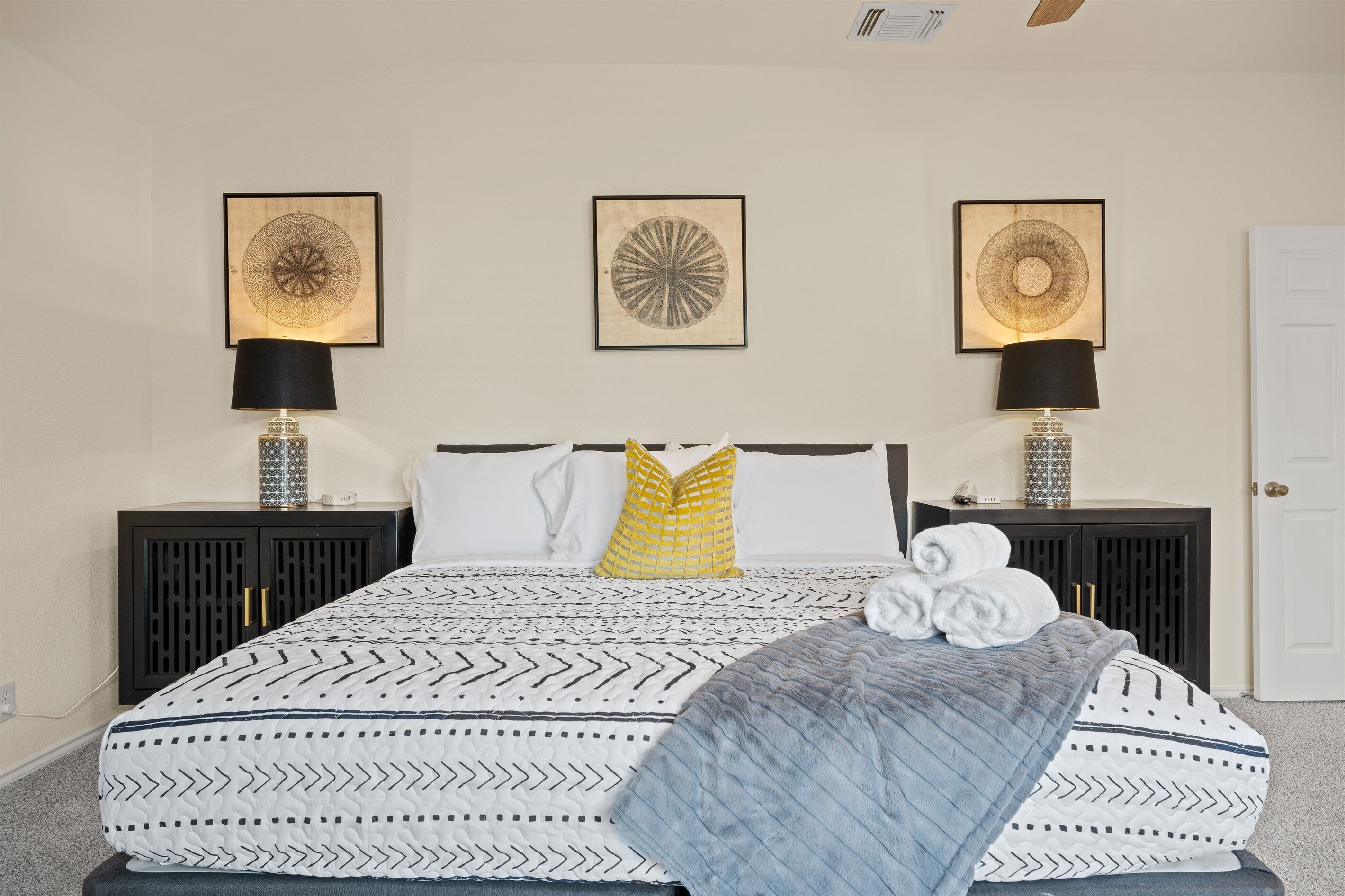 Une chambre à coucher bien aménagée, avec un grand lit, deux tables de chevet dotées de lampes et trois œuvres d’art accrochées au mur.