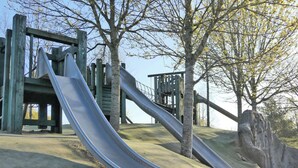 A playground with two slides, wooden structures, and trees. - 3 bedroom accommodation in Stirling (Stirling)