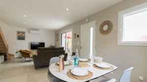 A modern living room with a sofa, a dining table set for two, and a television.