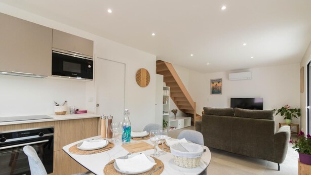 A modern kitchen with a built-in oven and microwave, a dining area with a table set for two, and a living room with a sofa and a TV.