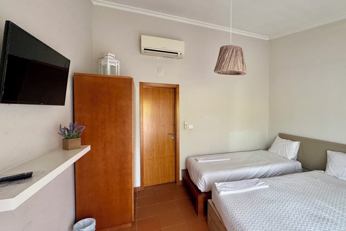 Une chambre d’hôtel avec deux lits, un téléviseur fixé au mur, un appareil de climatisation et une lampe suspendue.
