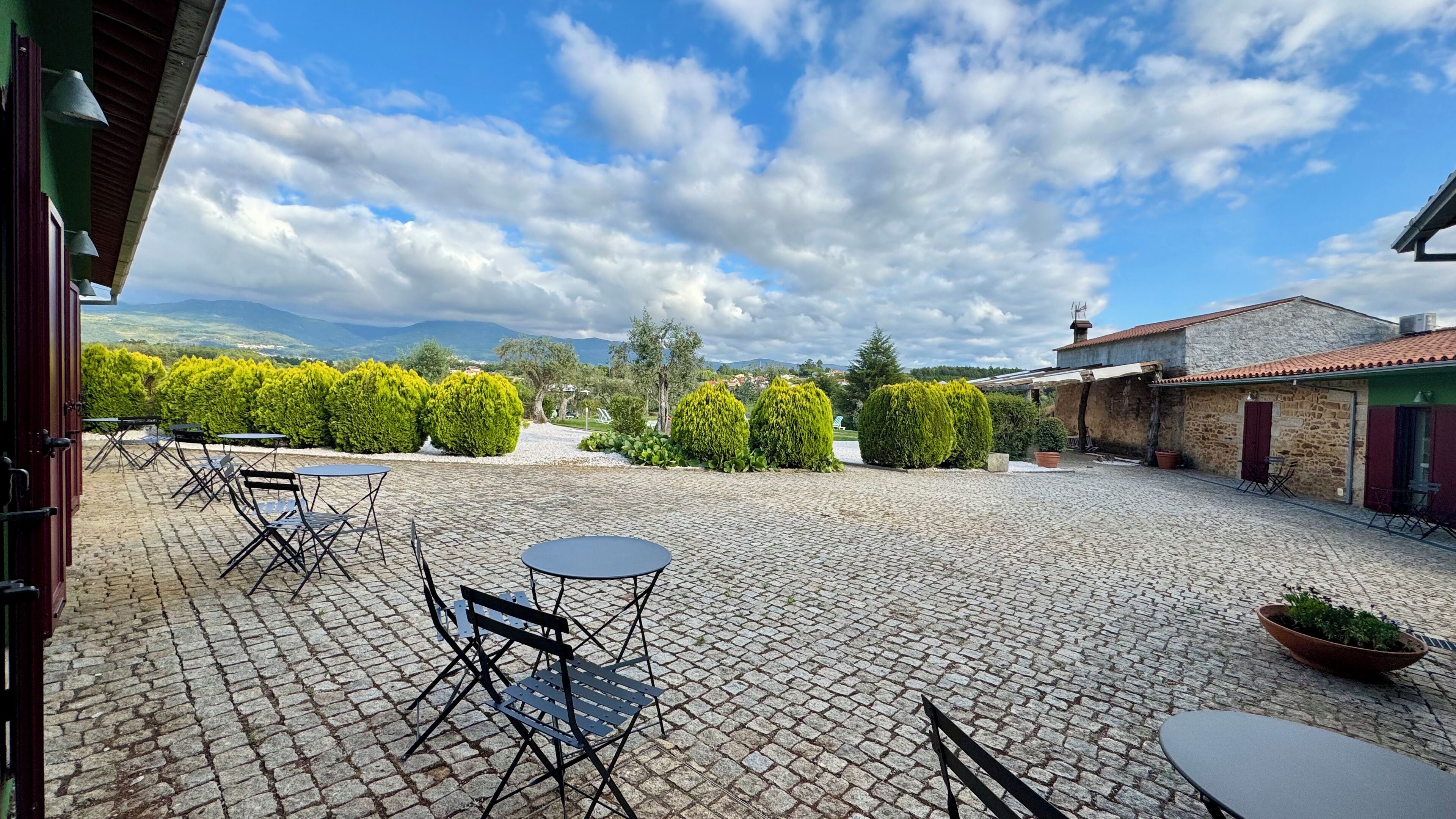 A courtyard with cobblestone flooring, outdoor seating, and a view of distant mountains.