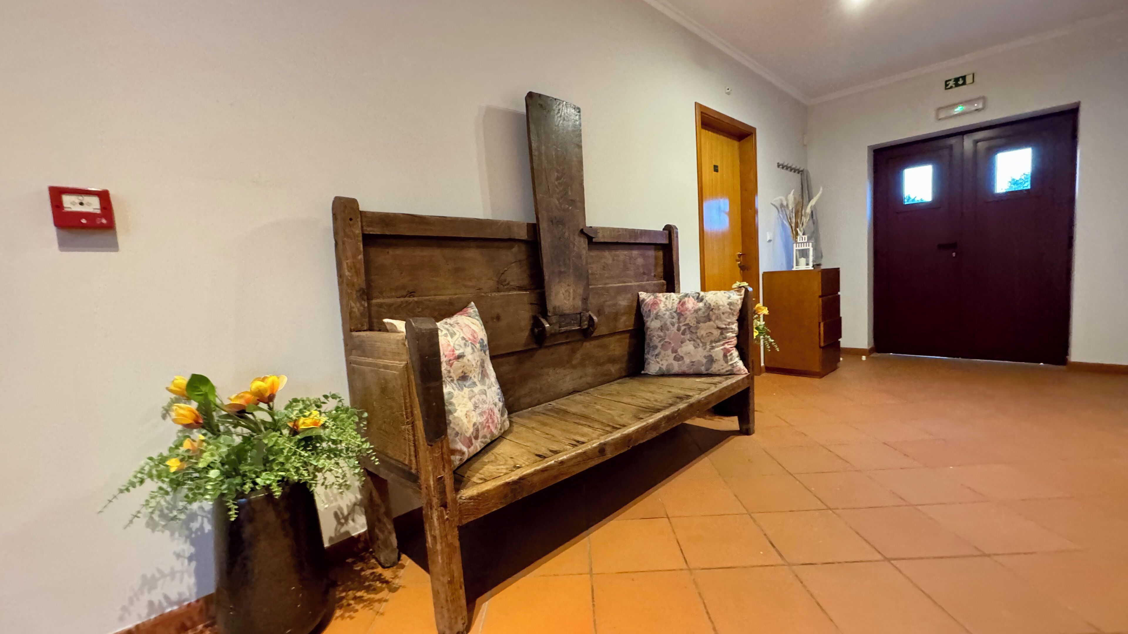 A wooden bench with floral cushions in a hallway with tiled flooring and a wooden door in the background.