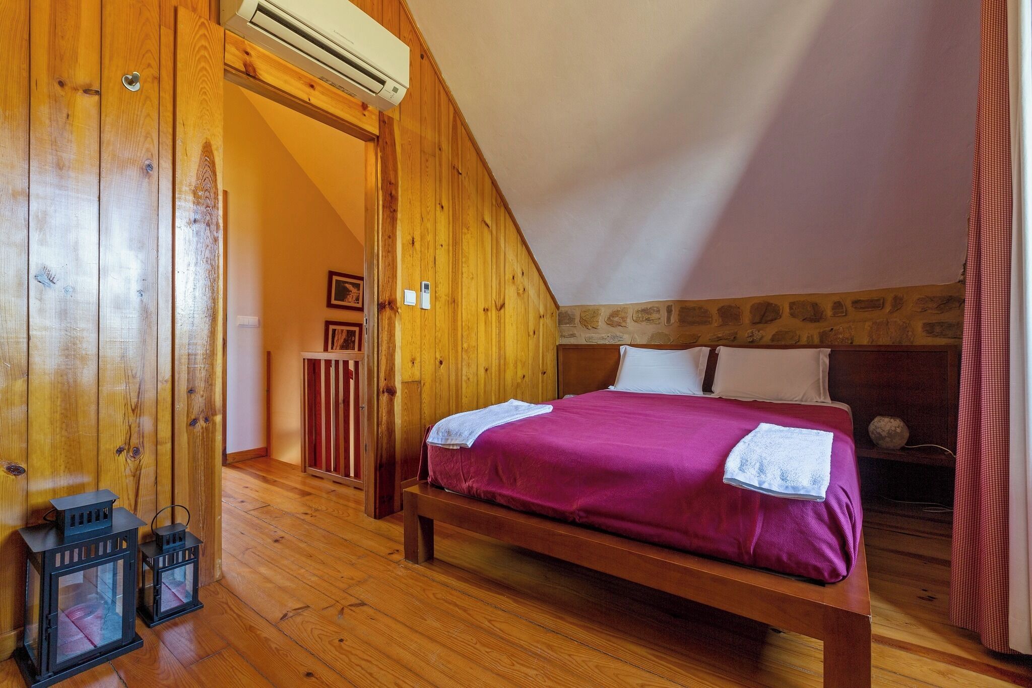 A bedroom with a wooden bed, a stone wall, and a wooden door.