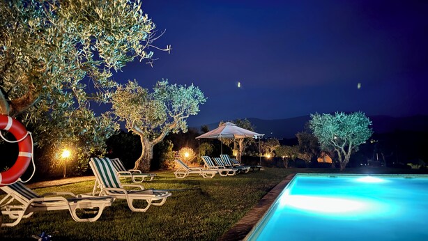 Ein Poolbereich mit Liegestühlen, einem Rettungsring und einem gut beleuchteten Schwimmbad bei Nacht.