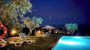 Zona de piscina con sillas de descanso, un flotador salvavidas y una piscina iluminada durante la noche.