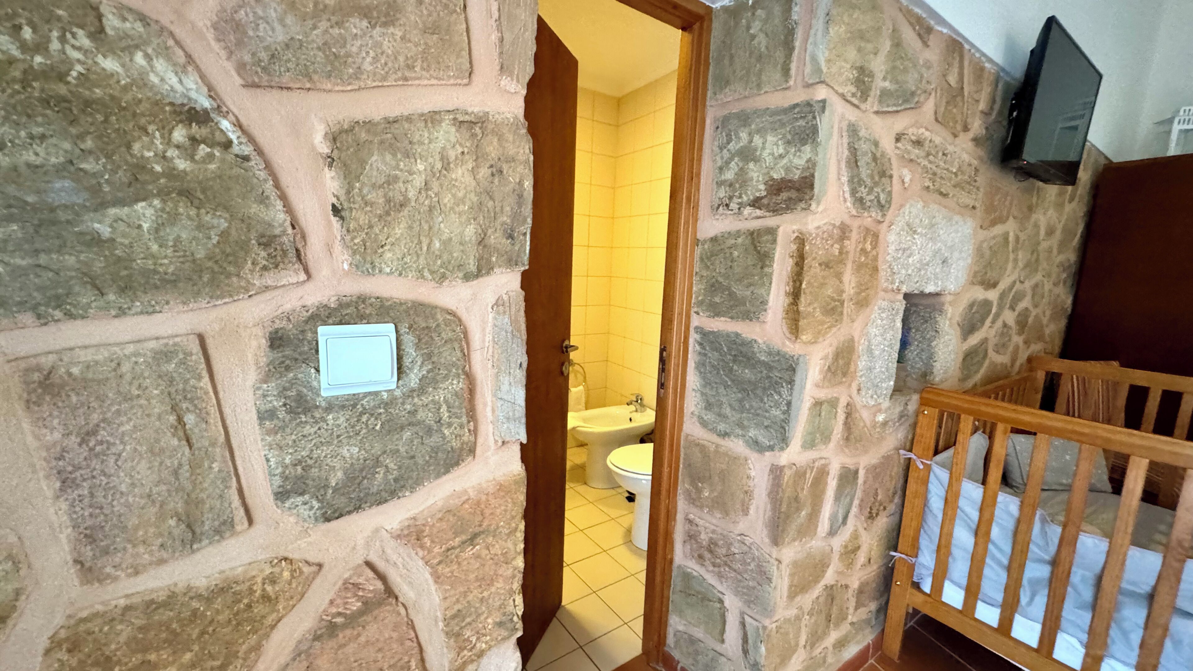 A stone-walled bathroom with a wooden bench and a white sink.