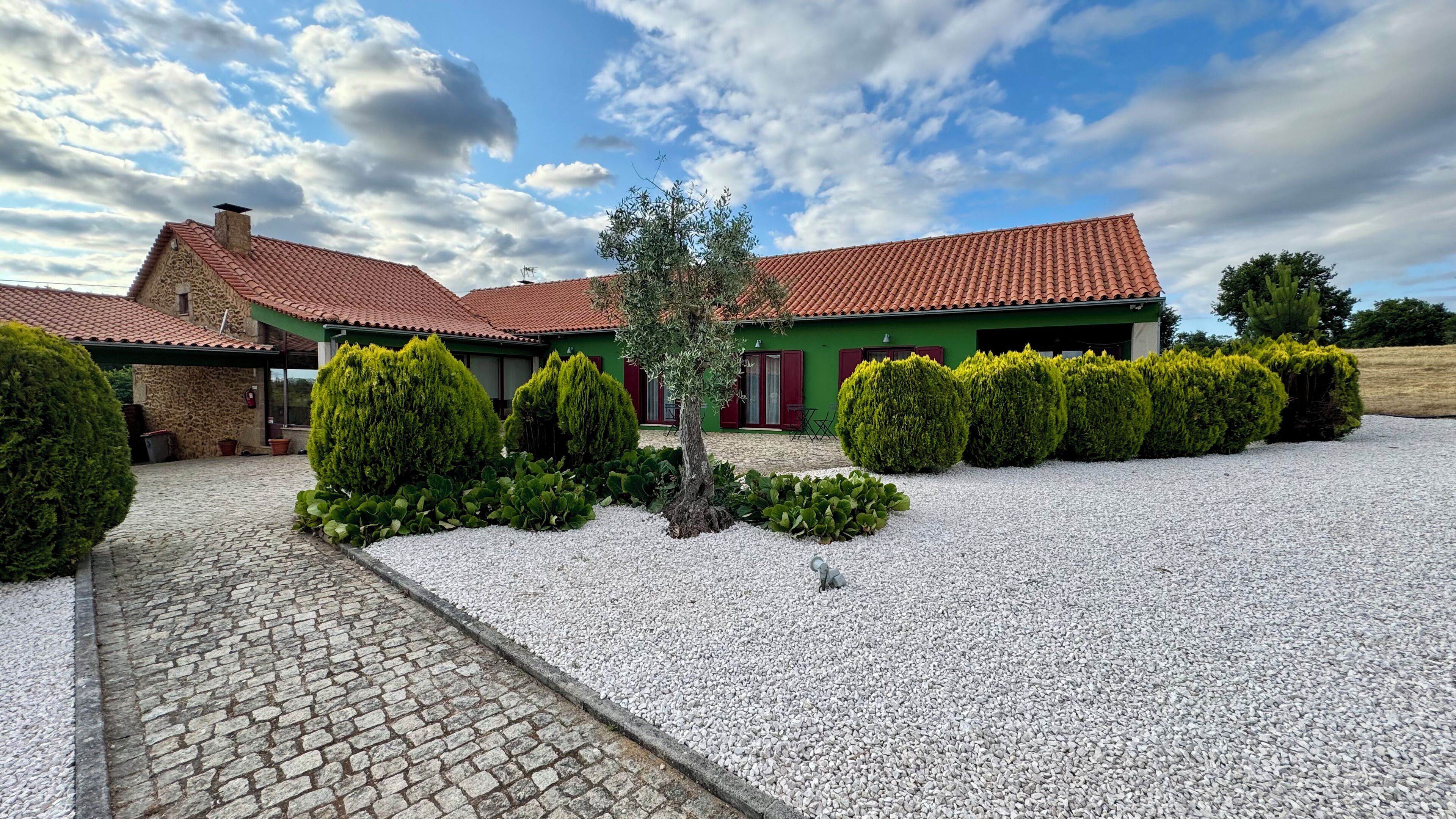 Una casa con techo de tejas rojas, paredes verdes y camino de entrada de grava.
