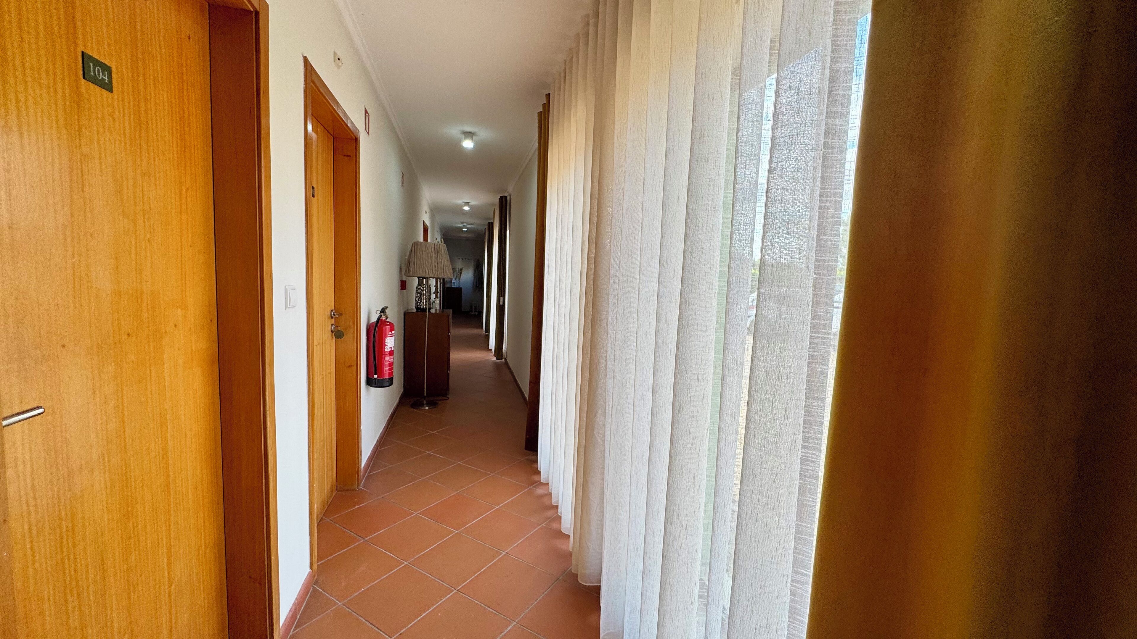 A hotel corridor with wooden doors, a fire extinguisher, and a lamp.