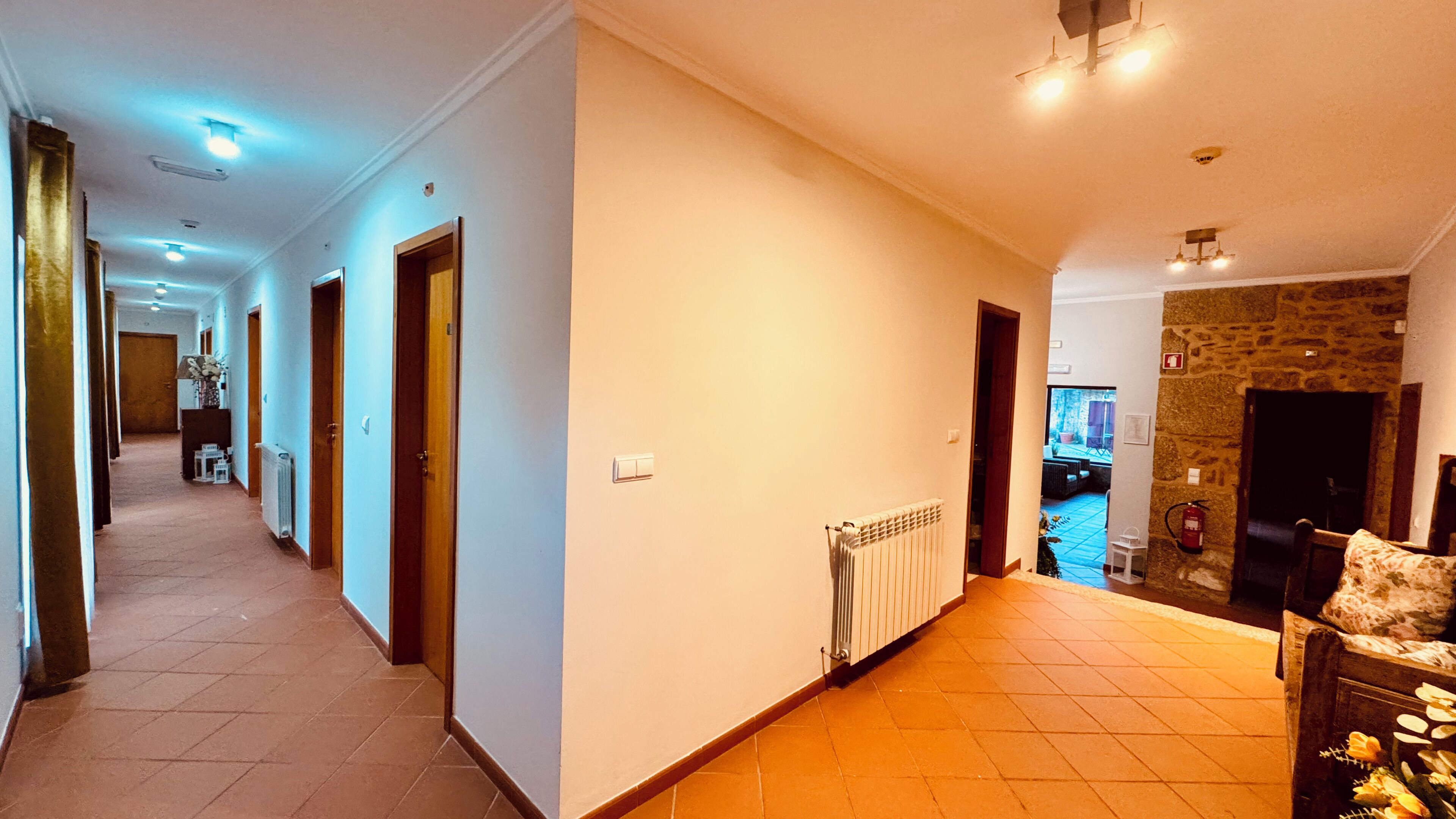 A hotel hallway with multiple doors, a radiator, and a stone wall on the right.