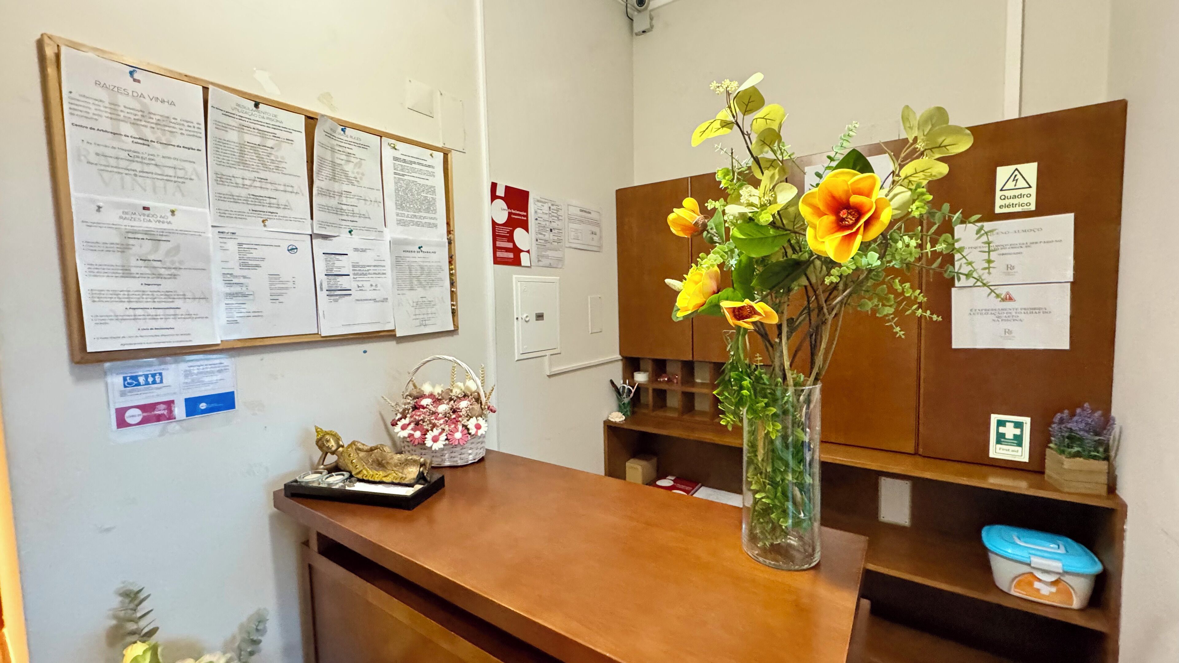 A reception desk with a bulletin board displaying various notices and a vase with flowers.