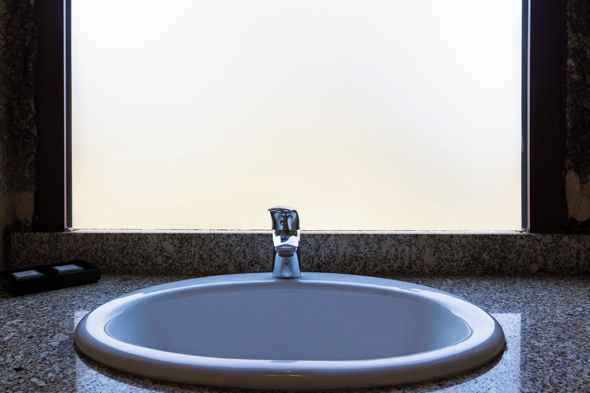A bathroom sink with a faucet, a window above it, and a granite countertop.