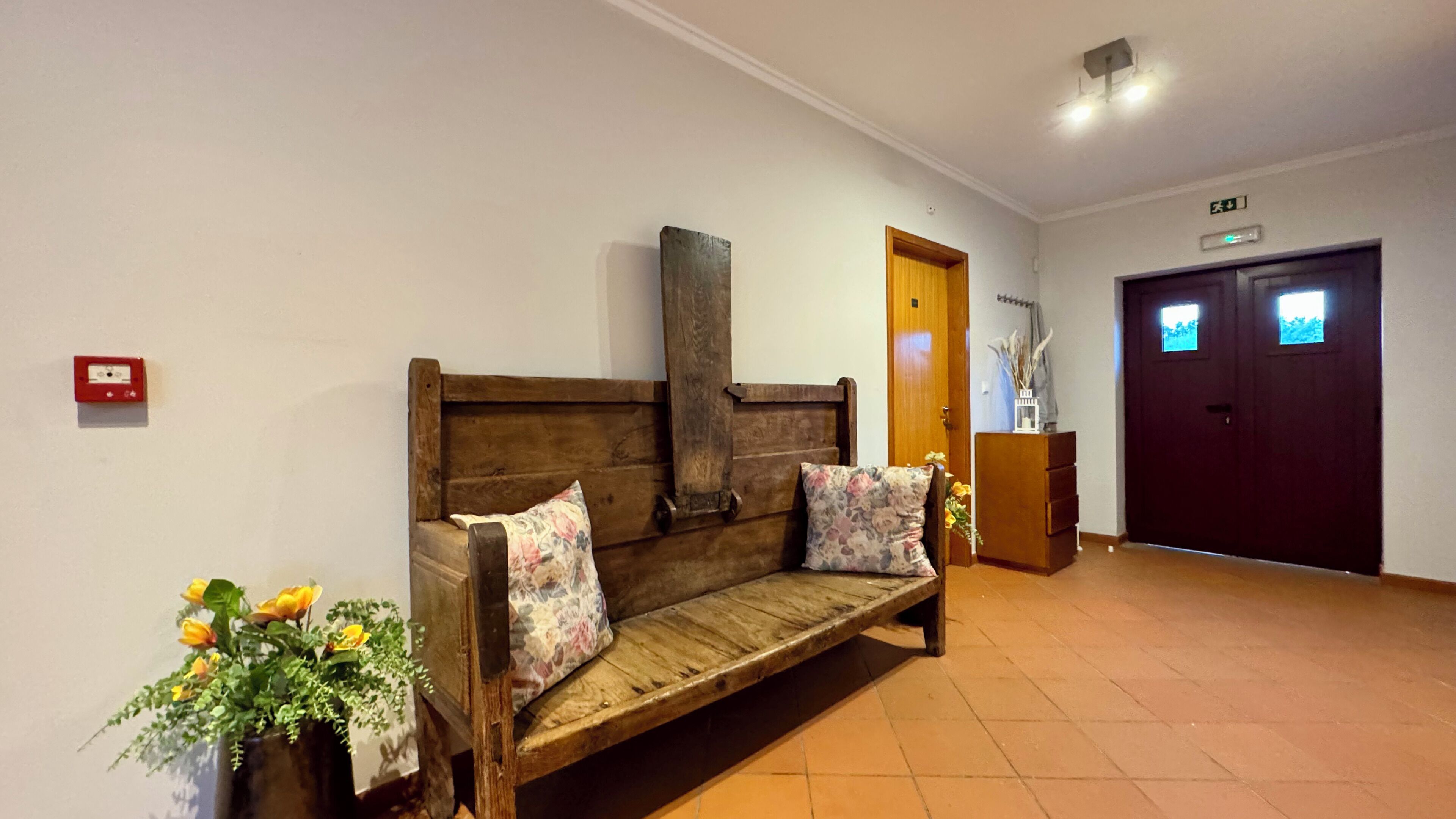 A wooden bench with floral cushions in a hallway with tiled flooring and a dark wooden door.