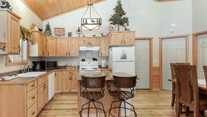 Una cocina con armarios de madera, estufa, refrigerador y dos sillas de metal.