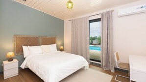 Un dormitorio con cama, mesitas de noche, escritorio y vista a una piscina.