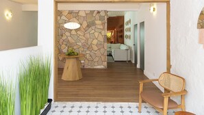 Un interior moderno con una pared de piedra, suelo de madera, una mesa redonda de madera con frutas y una silla de mimbre.