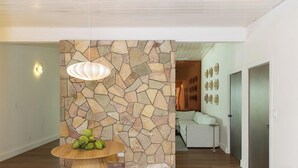 Un interior moderno con una pared de piedra, una mesa redonda de madera con fruta y una lámpara colgante.