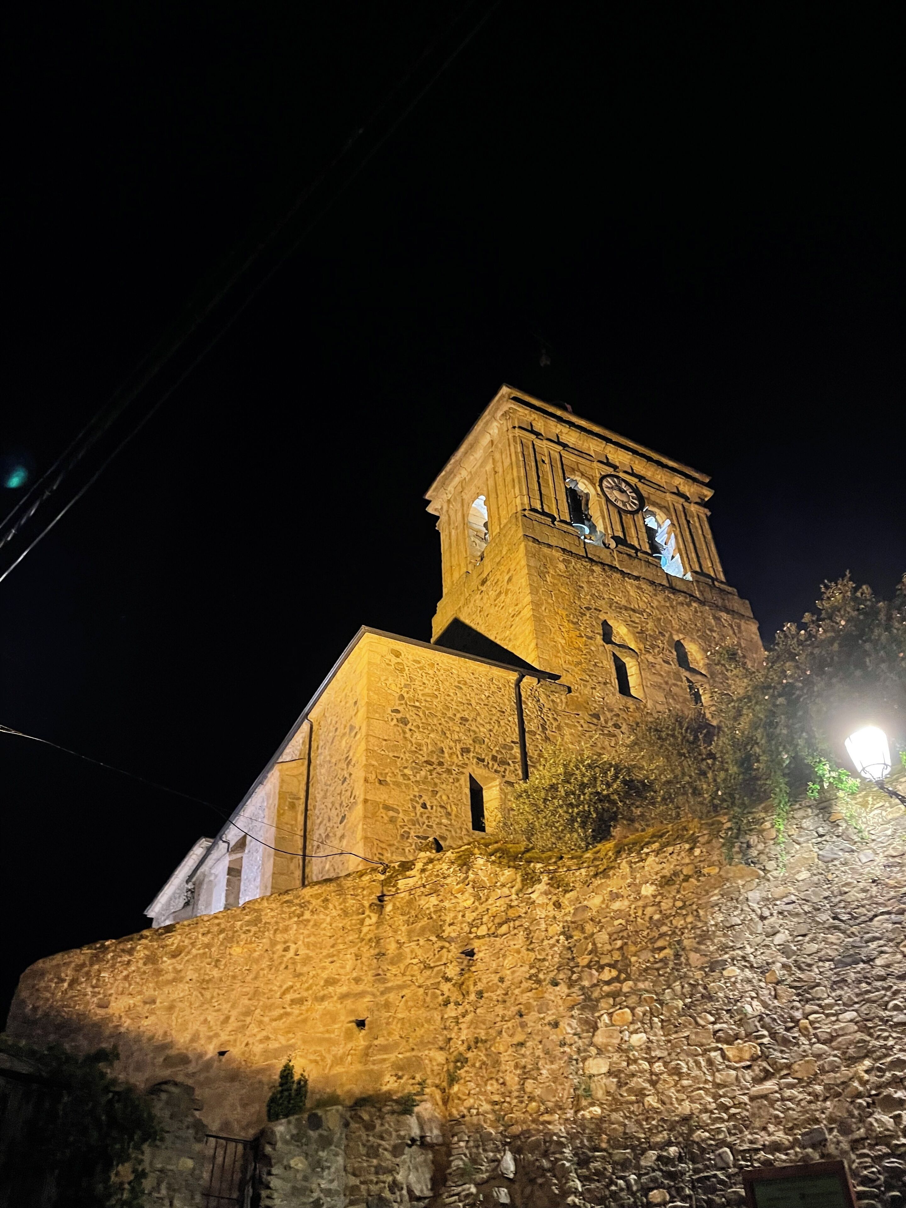Un edificio de piedra con una torre del reloj, iluminado durante la noche.