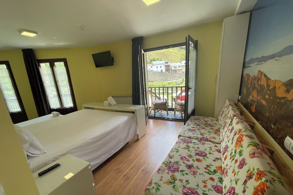 A hotel room with a bed, a sofa, a TV, and a balcony with a view of buildings.