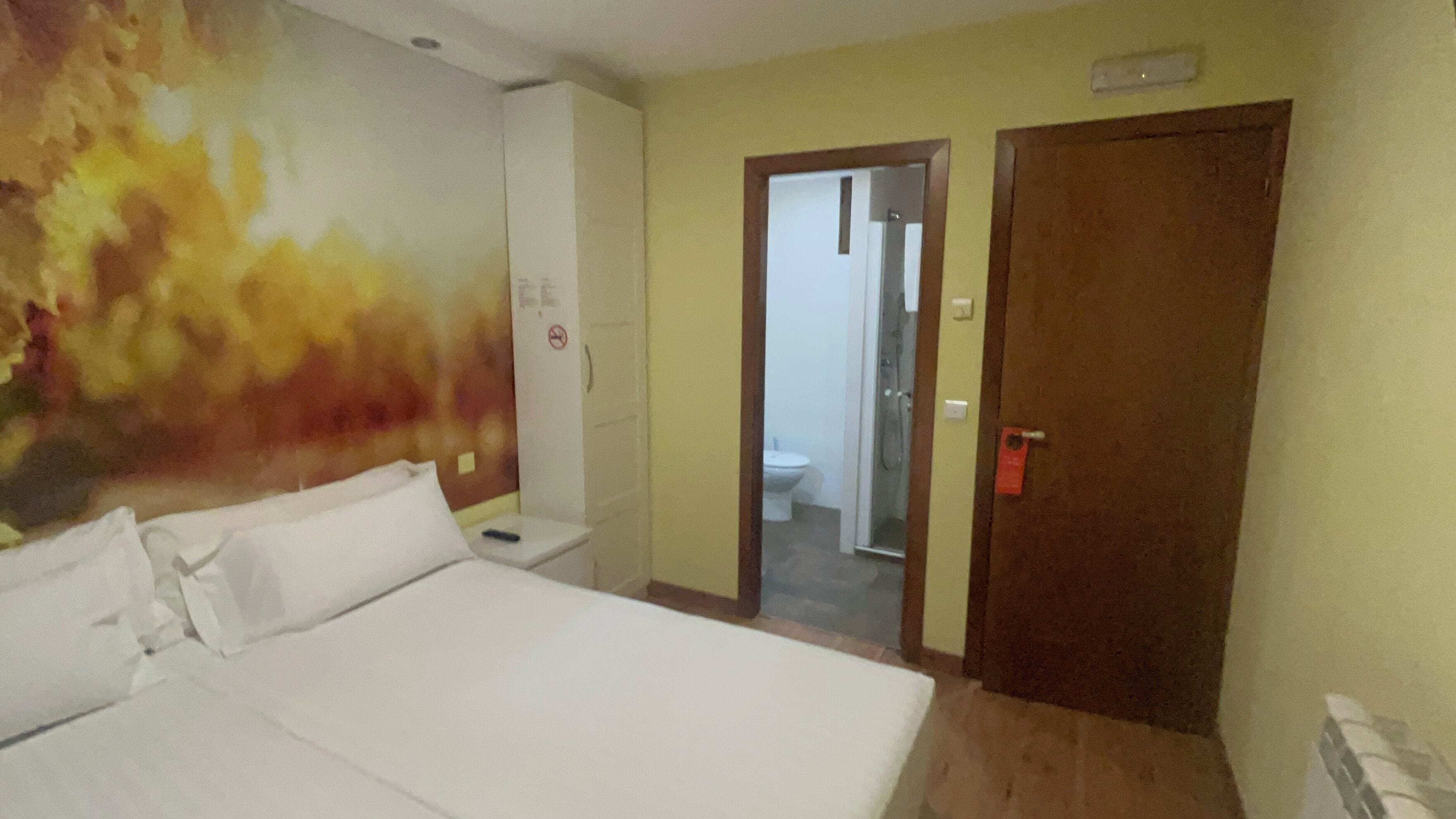Habitación de hotel con una cama grande, un baño visible a través de una puerta abierta, y una pared decorada con un mural texturizado.