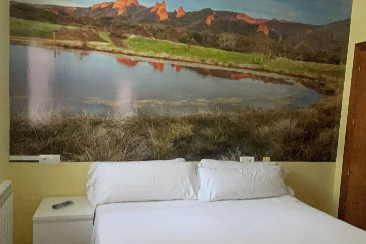 A bedroom with a bed, a nightstand, a rolled towel, and a large landscape painting on the wall.