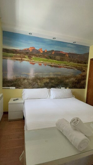 A bedroom with a bed, a nightstand, a rolled towel, and a large landscape painting on the wall. - THE WAY HOTEL & SUITES (Molinaseca)