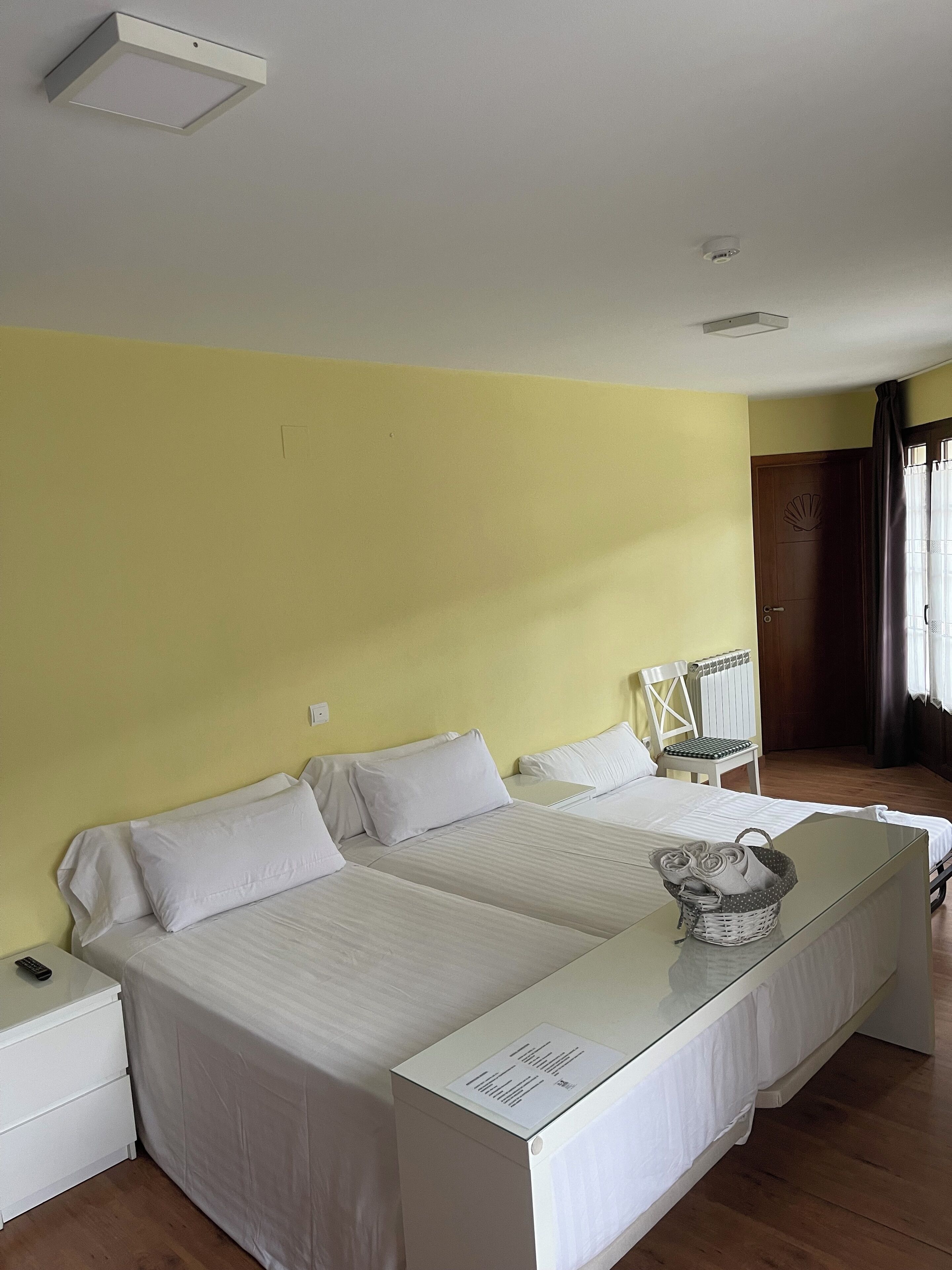 Habitación de hotel con dos camas individuales, una mesita, una silla y una ventana con cortinas.