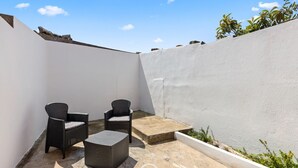 A small outdoor patio area with two wicker chairs and a square table, surrounded by a white wall and a concrete floor. - La casa di Amelie - Cabras (Cabras)