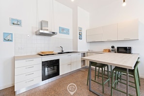 Eine moderne Küche mit weißen Schränken, einer Edelstahl-Dunstabzugshaube, einer Mikrowelle und einem Holztisch mit grünen Stühlen.