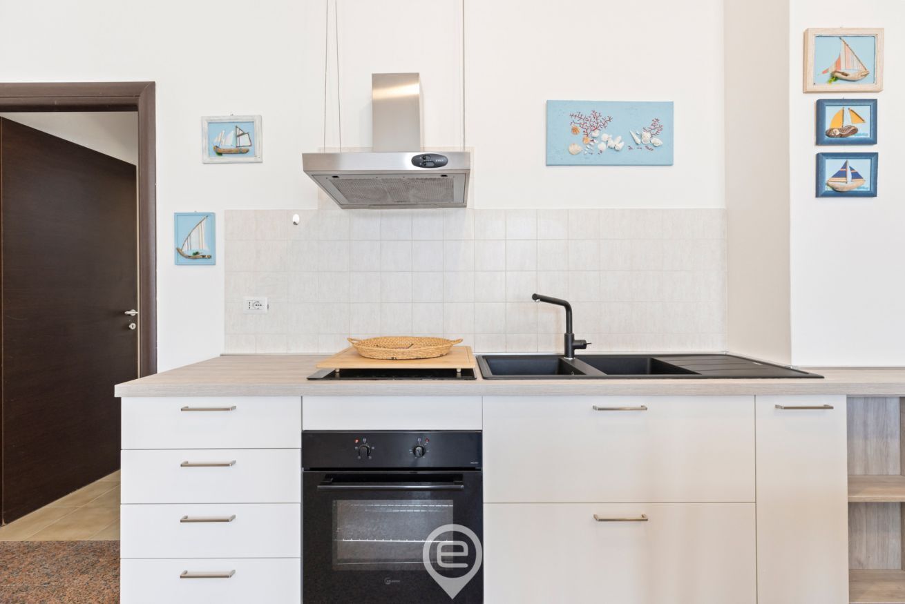 Una cocina moderna con armarios blancos, una campana extractora de acero inoxidable, horno integrado y lavavajillas negro.
