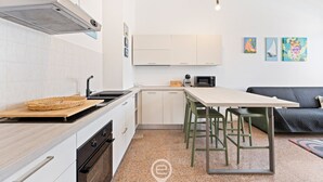 A compact kitchen with white cabinets, a microwave, a stove, and a dining area with a table and chairs. - La casa di Amelie - Cabras (Cabras)