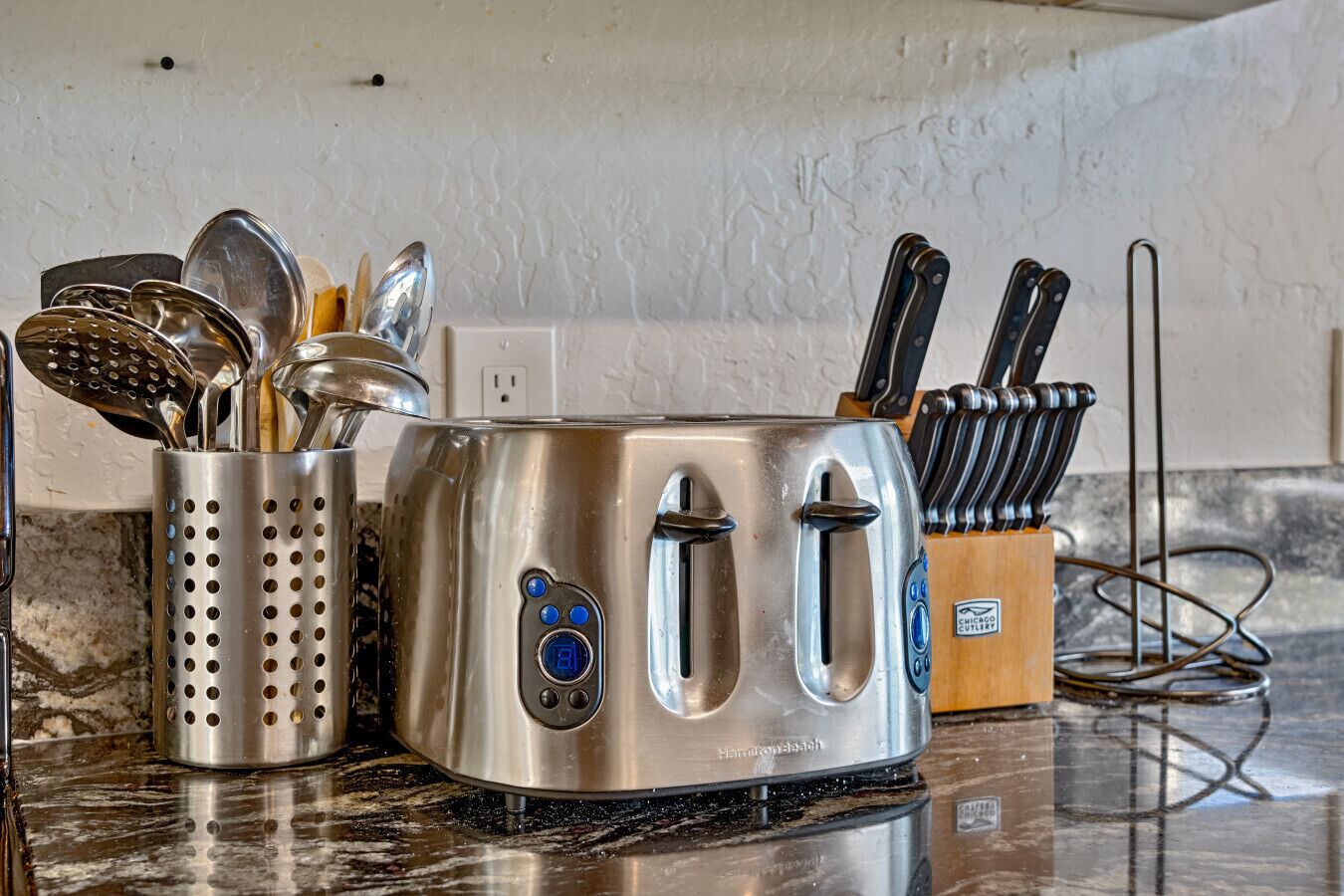 A kitchen with a stainless steel toaster, a colander, and a knife block.