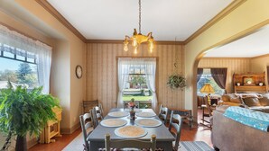 Un comedor con una mesa dispuesta para seis personas, rodeada de sillas, una araña y vistas a un jardín a través de una ventana.