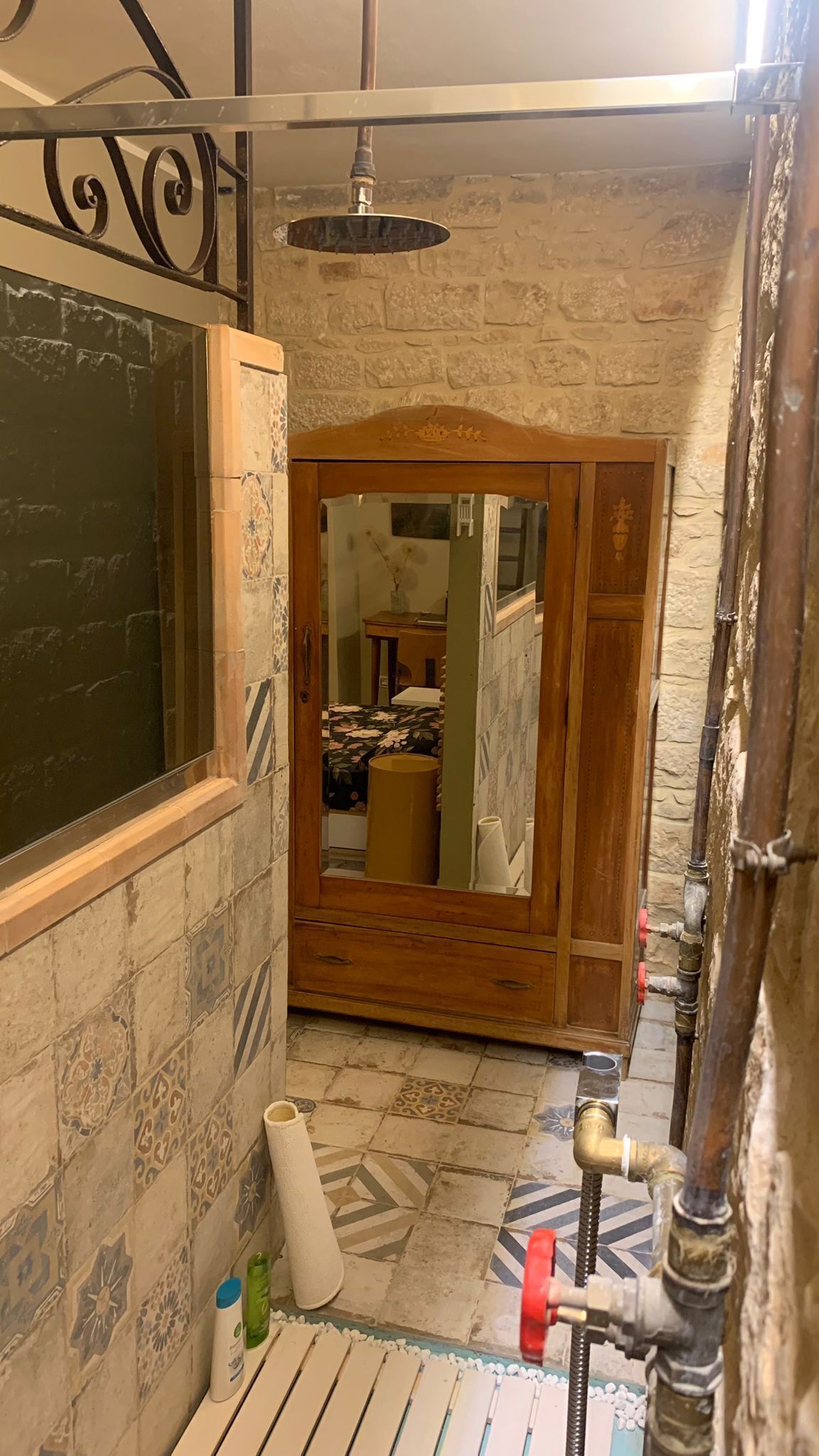 Ein schmaler Flur mit einer Holztür, die in ein Schlafzimmer führt, mit gefliesten Wänden und einem sichtbaren Wasserrohr.