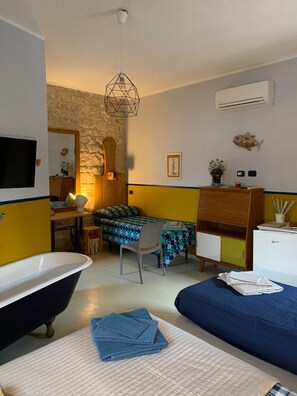 A bedroom with a bed, a desk, a chair, a vanity with a mirror, a bathtub, and an air conditioning unit. - Richiami di Sicilia (Modica)